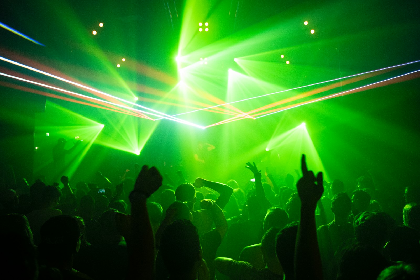Dark warehouse rave with green laser beams cutting across the room over a crowd with their hands in the air, the kind of high-energy room drum and bass is built for