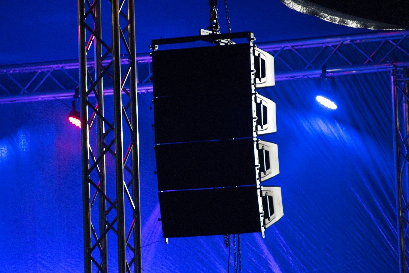 A hanging line-array speaker stack lit in deep blue and red stage light, the kind of bass rig a dubstep drop is built to move
