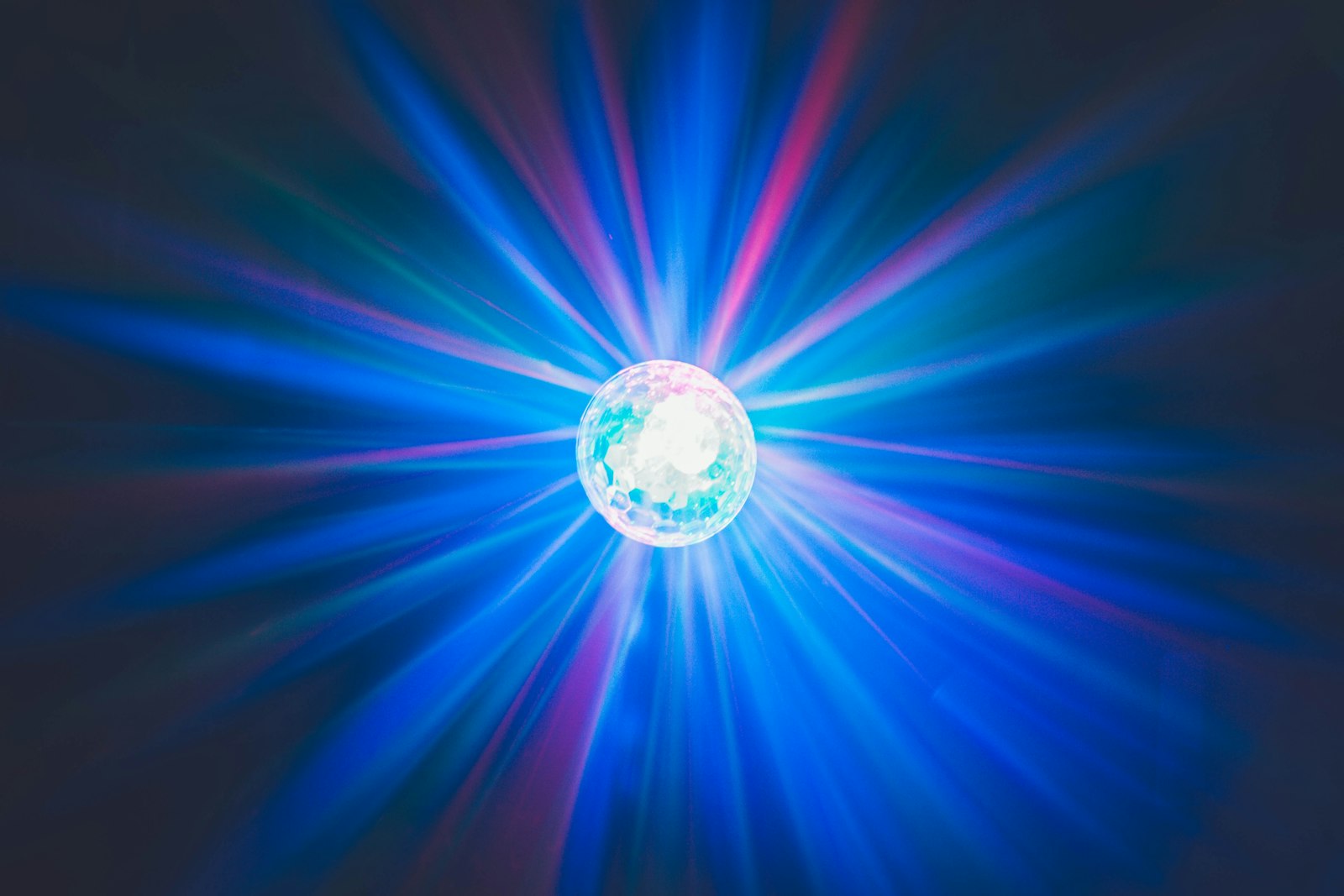 A bright disco strobe light throwing blue, pink and green beams out across a black room, the kind of fast flashing light a flickering visualizer recreates on screen