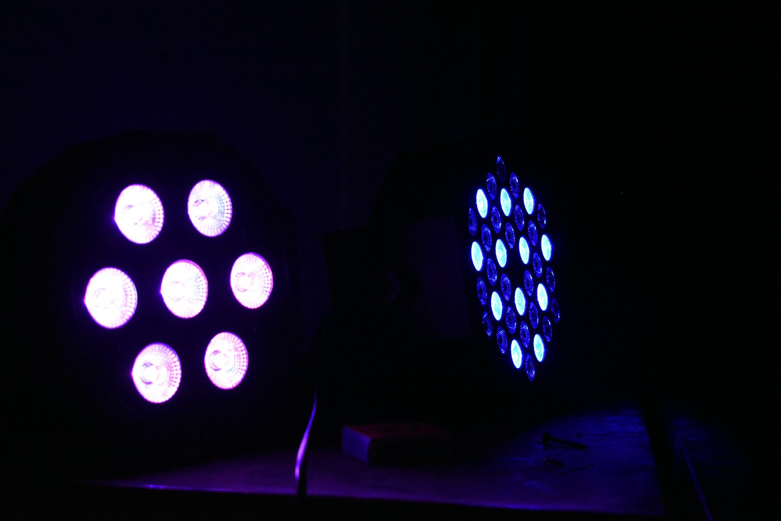 Two LED stage light fixtures glowing white and blue in a dark room, the kind of hard flashing light a strobe video imitates on screen