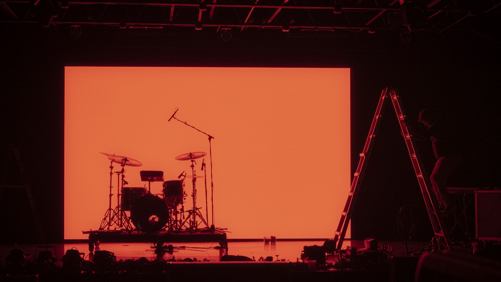 A drum kit set up on a dark stage in front of a large glowing orange LED video wall, the kind of screen a live performance visualizer plays behind a band