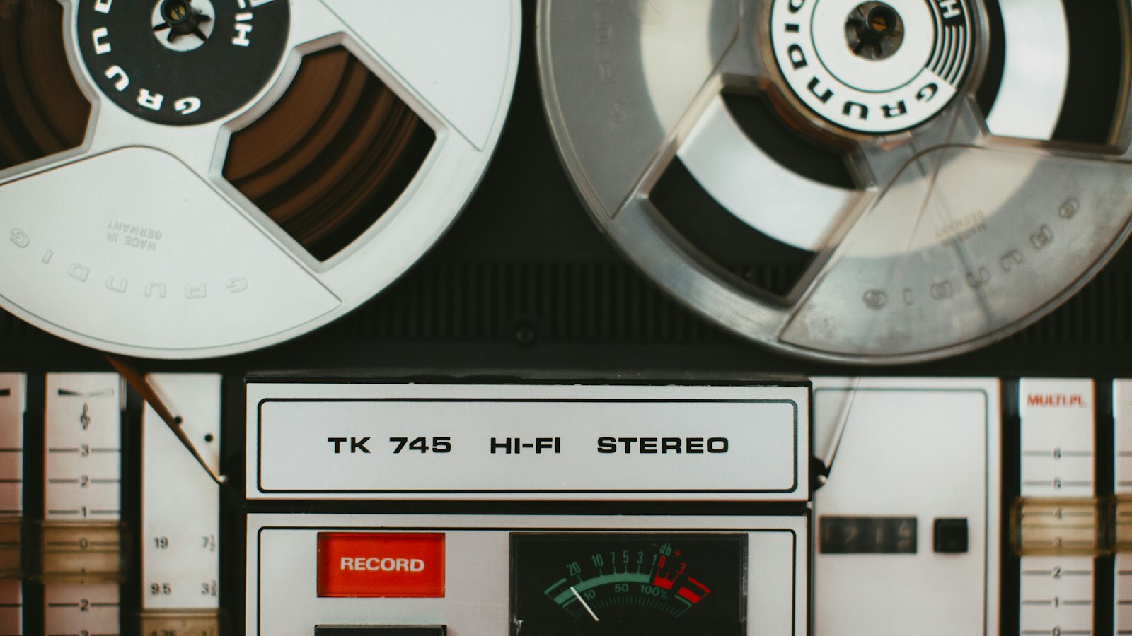 Close view of a Grundig TK 745 reel to reel tape deck with both reels loaded, a red record button and a VU meter