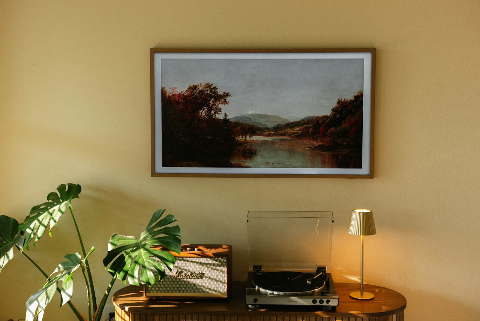 A single framed landscape picture hanging in a warm lit room above a turntable and a speaker, one still image with a record playing underneath it