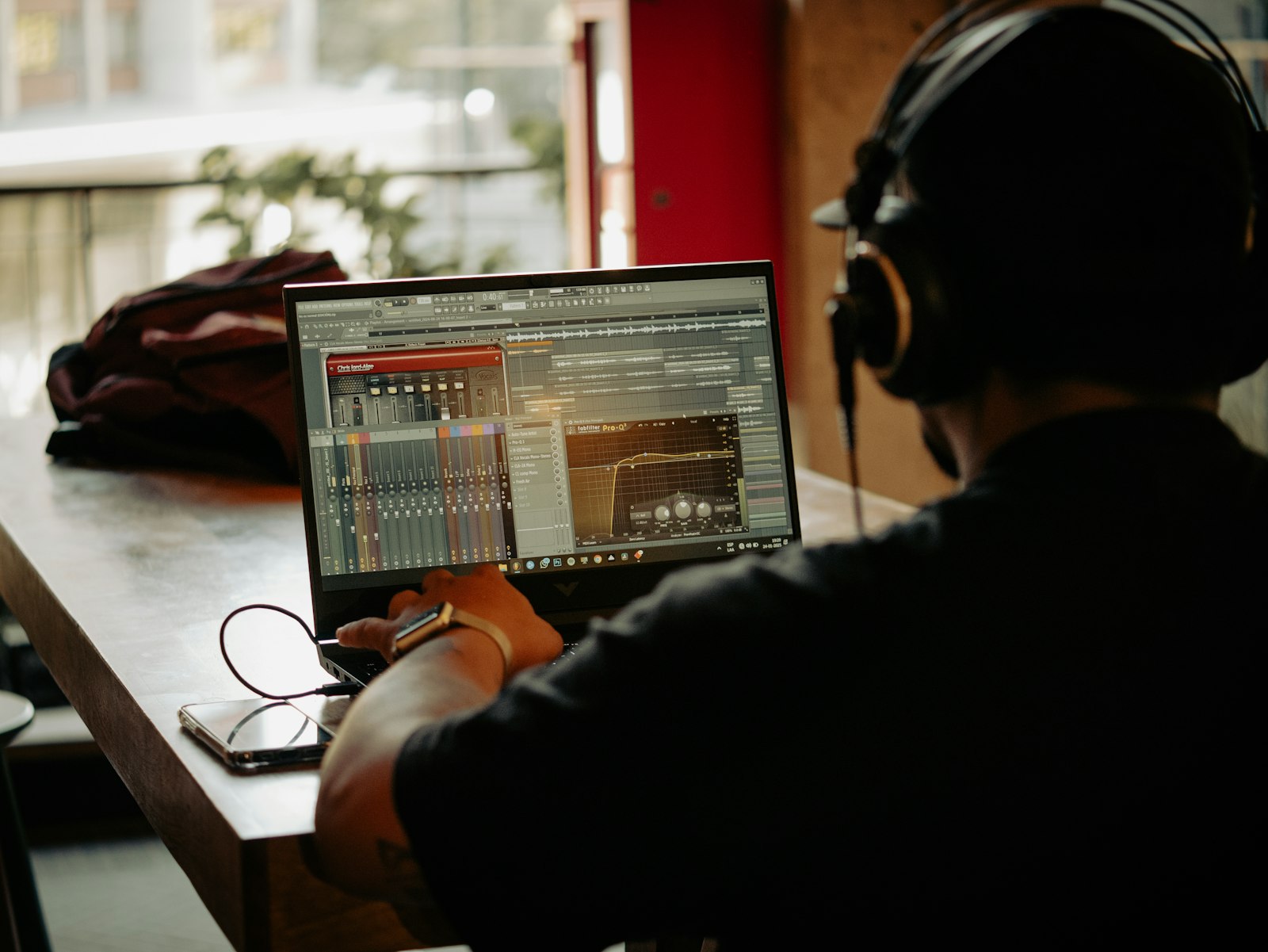 A music producer wearing headphones working on a beat in a DAW on a laptop, the kind of session a type beat visualizer video gets built from