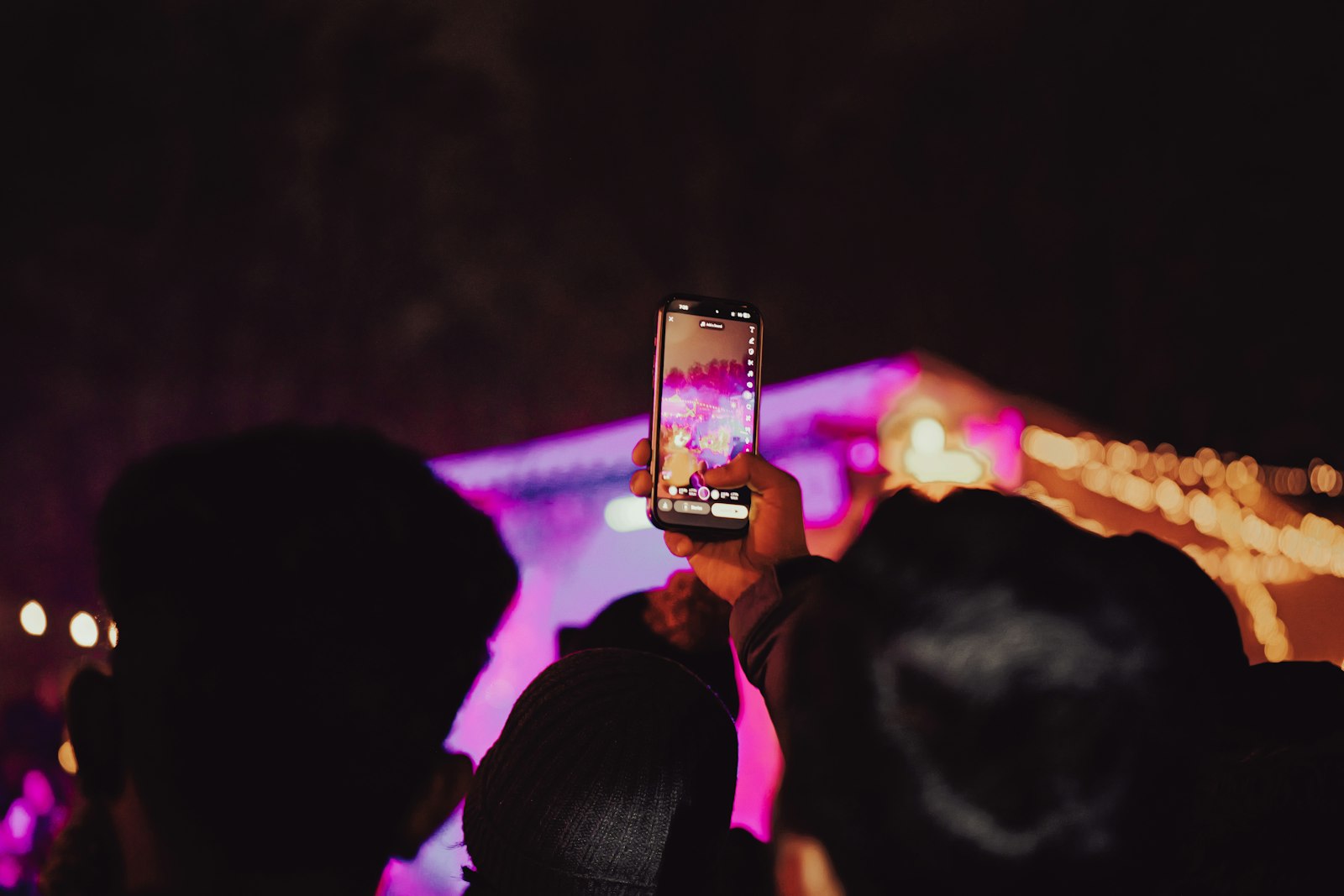 A phone held upright at a night show, its screen filled with a vertical capture of the stage and the app's own interface stacked down the edges