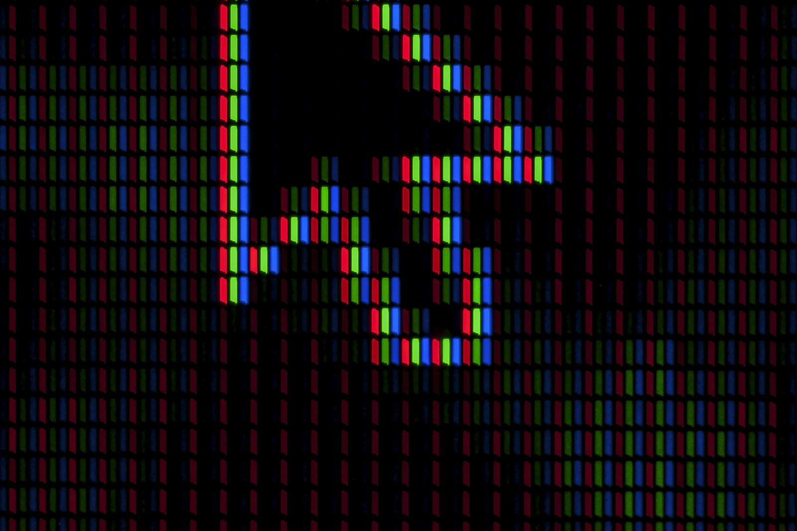 A macro photograph of a screen's red, green and blue subpixel stripes, with a mouse cursor arrow picked out in lit pixels against the dark panel
